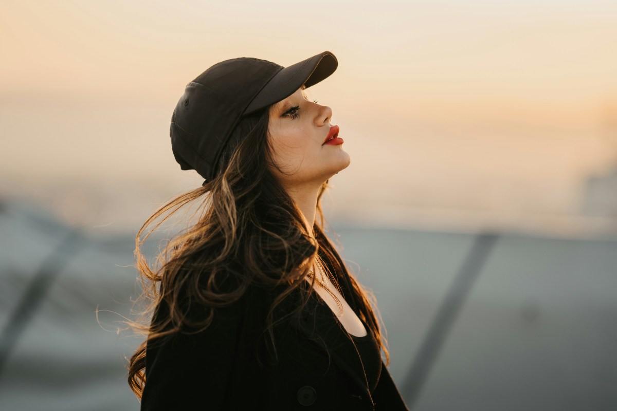 Ragazza di profilo che indossa un cappotto e un cappello da baseball. Tramonto sullo sfondo
