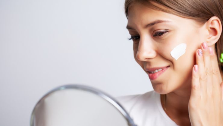 Donna applica crema sul viso davanti allo specchio